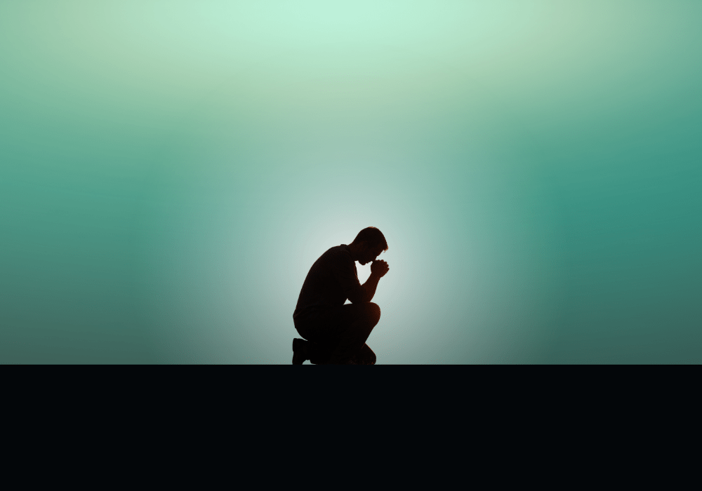 Silhouetted man kneeling to pray against a neon green horizon